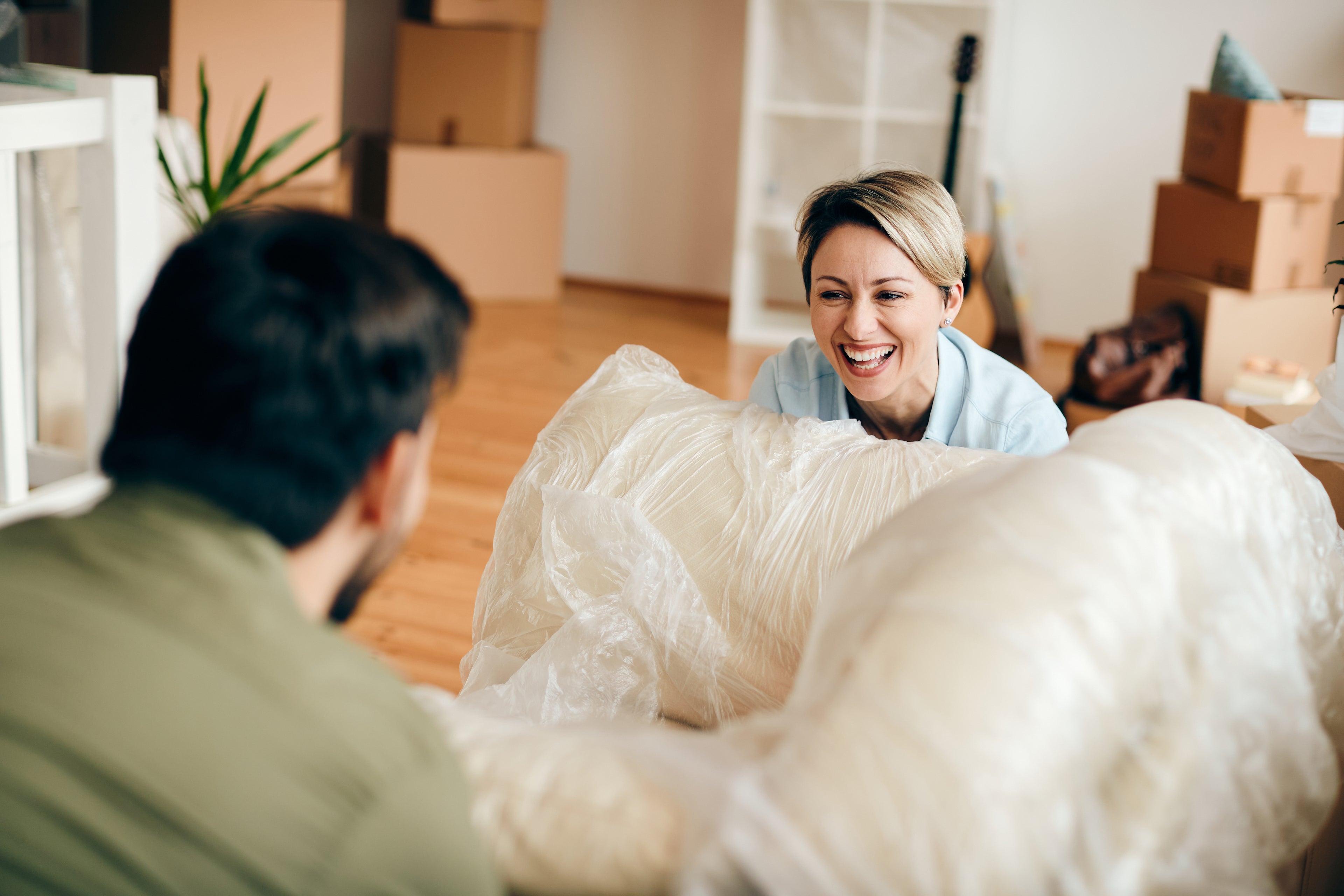 Two people unpacking furniture in a room with boxes and a guitar in the background