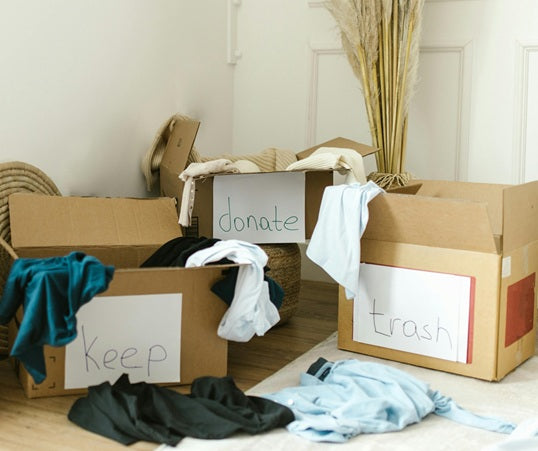 Three cardboard boxes labeled 'keep', 'donate', and 'trash' with clothes inside on a wooden floor.